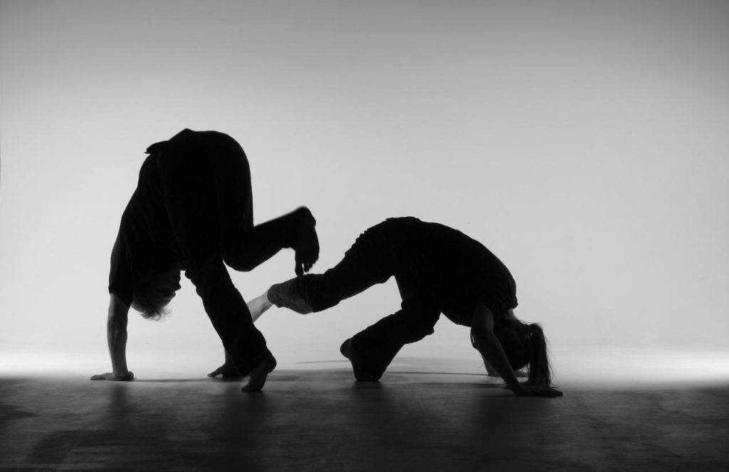 Two Capoeiraplayers as dark silhouette against a lighter background.